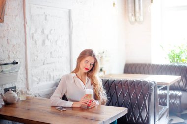 Kafede otururken kahve tutan genç güzel uzun saçlı kadın.