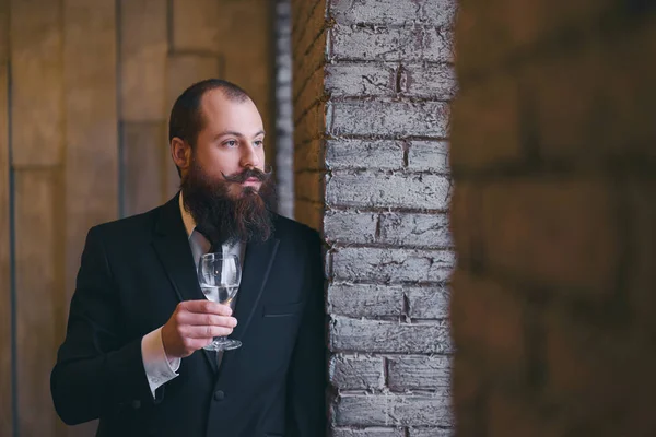 Adult successful elegant businessman with beard wearing suit and drinking wine.