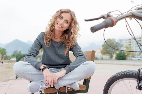 屋外のベンチの上に座ってカール長髪の素敵な笑顔の若い女性 — ストック写真