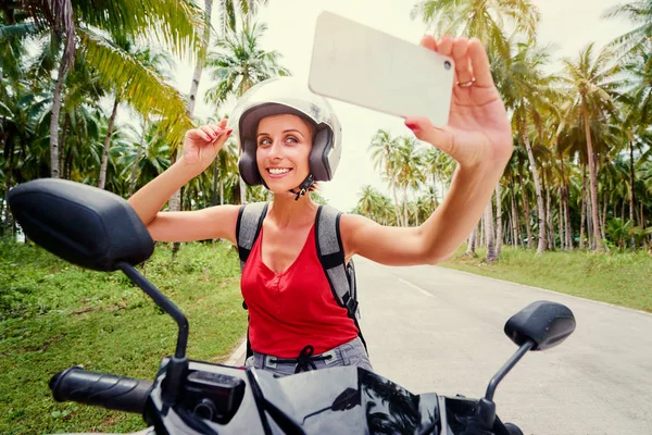 彼女のスマート フォン Selfie を取ってスクーターの上に座ってヘルメットでかなり若い女性の屋外のポートレート — ストック写真