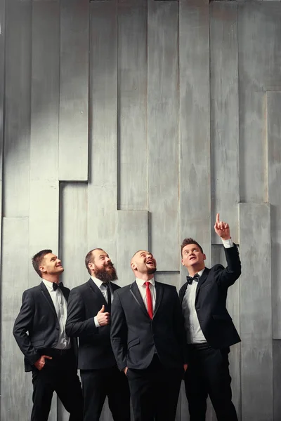 Group of interested business people looking up. Four elegant young men wearing tuxedo.