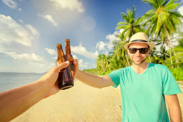 Young smiling man drinking beer with friend on the sea shore.