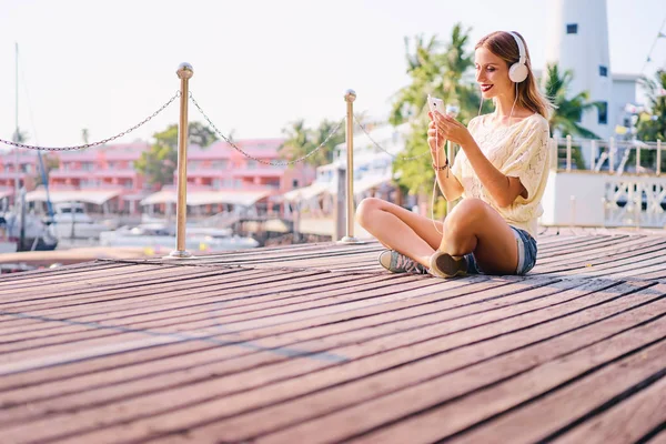 イヤホンで幸せな若い女海洋ハーバー デッキ ブロードウォークに座って音楽を聴くは — ストック写真
