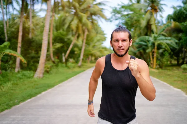 Young strong man is running under palm trees.
