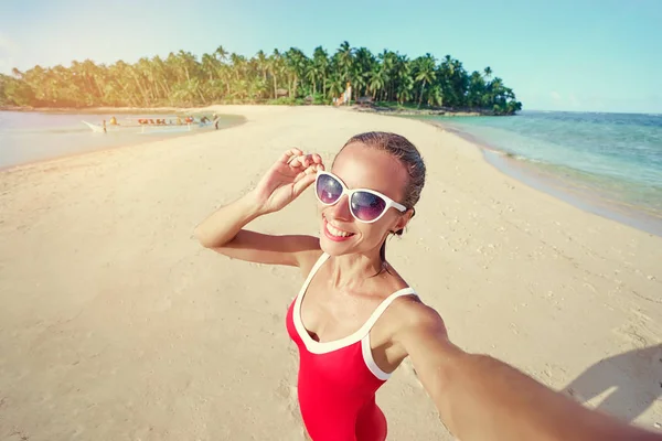 穿着红色泳装的漂亮年轻女子带着自拍在白沙热带海滩上 — 图库照片