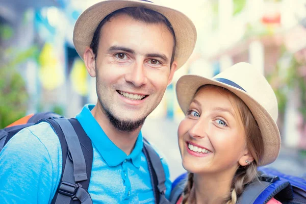 Close up portrait of traveling couple in hats with rucksacks.