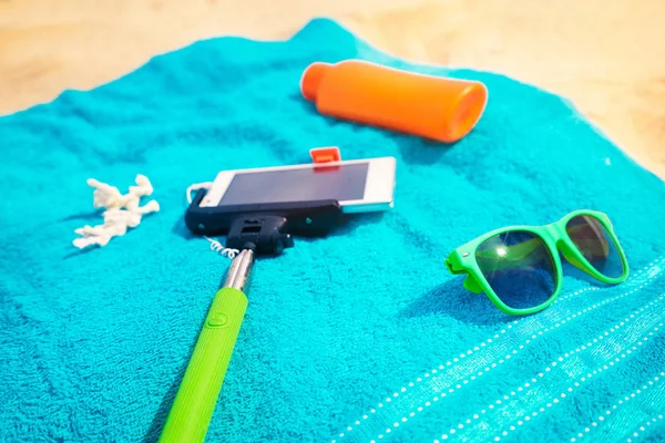 Must have accessories on the sea beach. Smartphone, selfie stick, sunscreen and sunglasses. Top view.