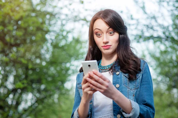 惊奇的年轻妇女使用智能手机在绿色公园 — 图库照片