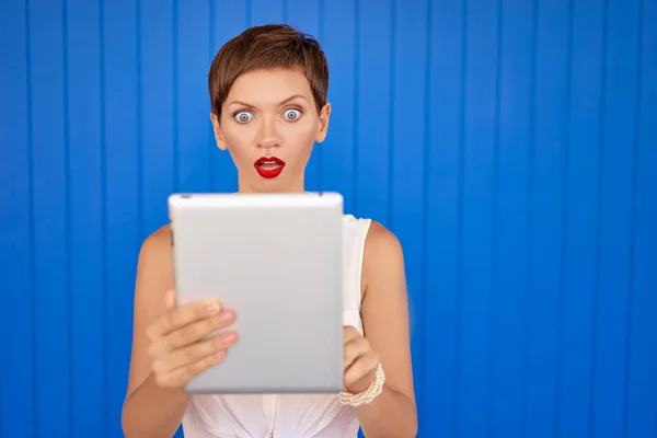 年轻漂亮的女人使用蓝色墙上的平板电脑的彩色画像 — 图库照片