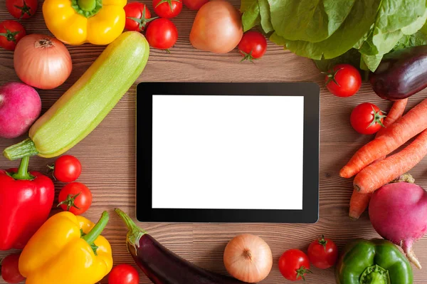 Tablet pc and ingredients for cooking vegetables over wooden background