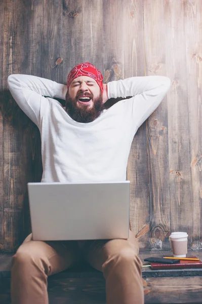 Yawning bearded man with laptop computer sitting over wooden background.