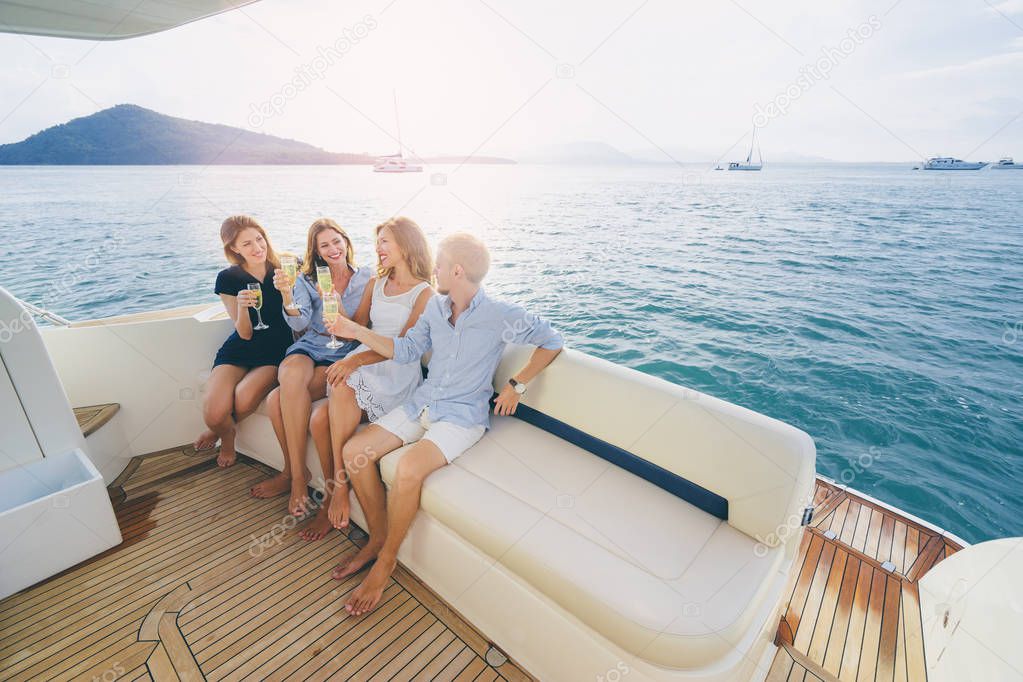 Group of laughing young people sitting on the deck drinking champagne sailing the sea.