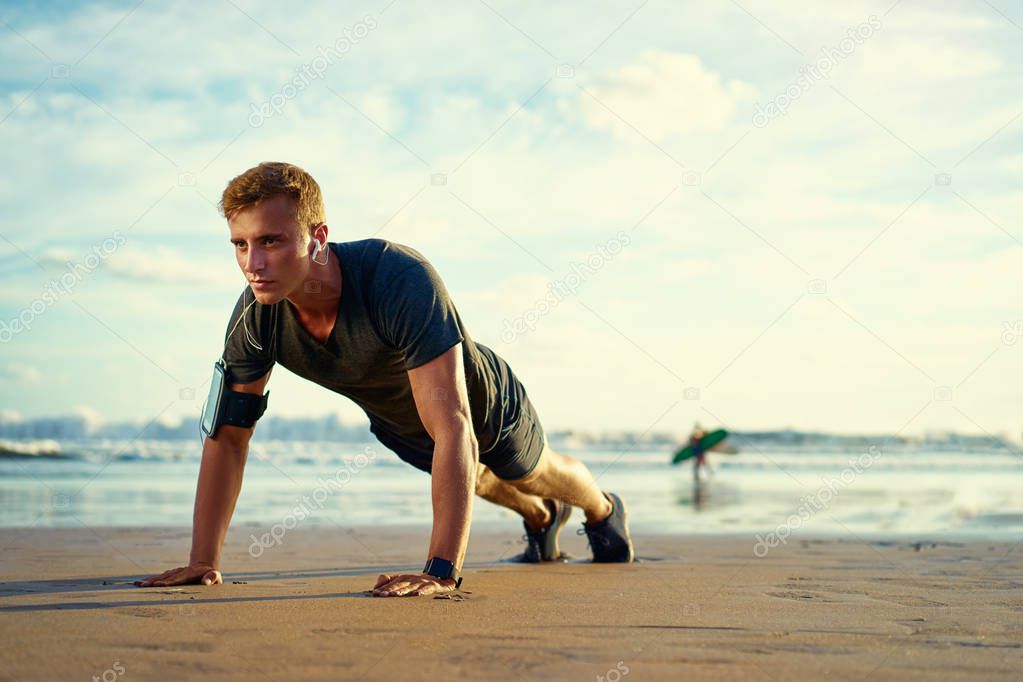 Young man doing push-ups on the ocean beach.