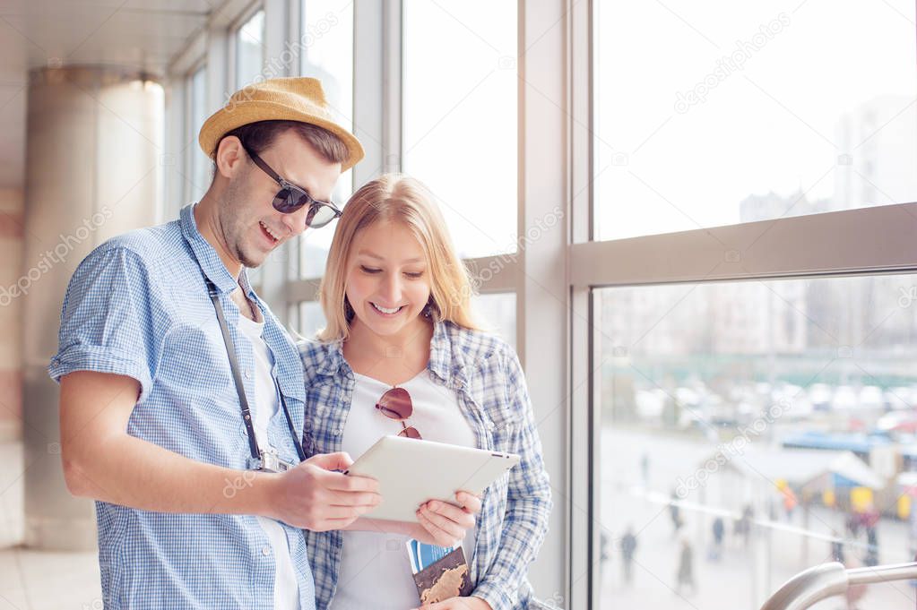 Young loving couple in casual wear using tablet computer while standing in the airport terminal waiting for boarding.