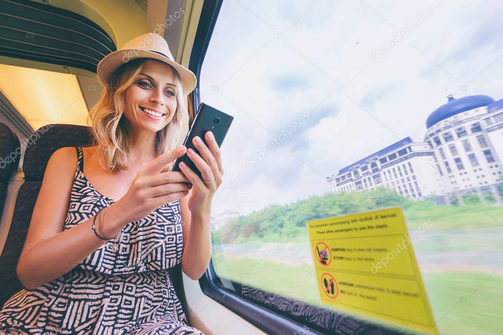 Young pretty woman traveling by the train sitting near the window using smartphone.