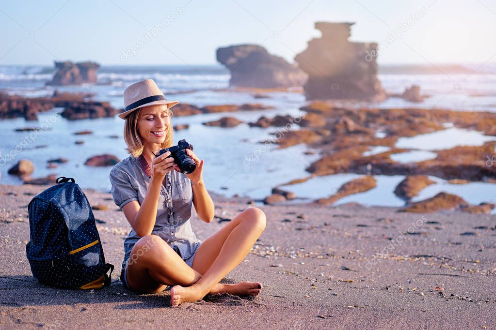 Pretty young woman with camera and rucksack on the ocean beach.