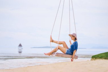 Mutlu genç kadın deniz manzarayı salıncakta oturan şapkalı.
