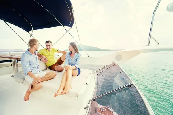 Group of laughing young people sitting on the yacht deck sailing the sea.