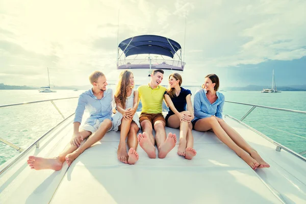Group of laughing young people sitting on the yacht deck sailing the sea.