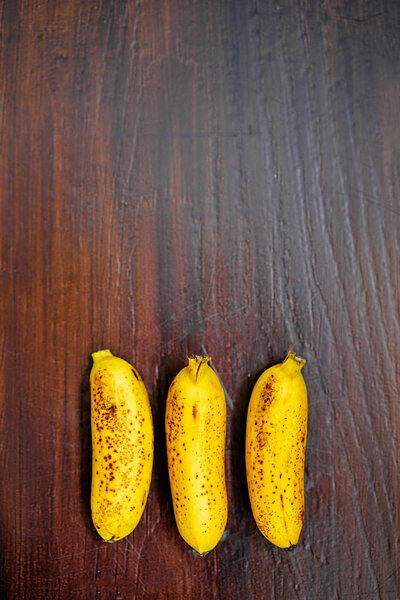 top view of three small bananas on wooden background.