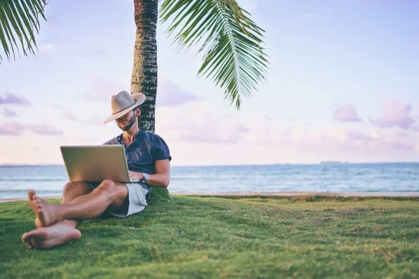 在棕榈树下热带海滩上的笔记本电脑工作的年轻人 — 图库照片