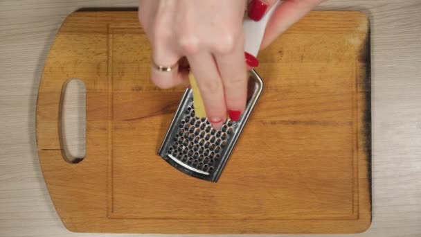 Vrouw raspen van de kaas op de keukentafel. Close-up van vrouwelijke handen kaas raspen. — Stockvideo