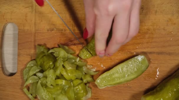 女人们的手在一块红色的切菜板上把切碎的腌制黄瓜切成小块，近距离拍摄。绿色的立方体反映在刀片上. — 图库视频影像