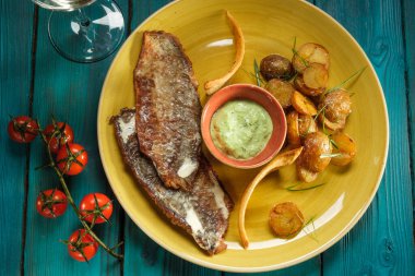 Kremalı soslu ızgara deniz sosu ve ahşap kaplamalı mavi ahşap arkaplanda fırında patates ve vişneli domates filizli pesto.