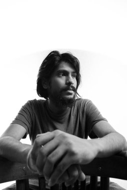 Hintli adam sandalyede oturuyor. Kameraya bakarak poz veriyorsun. Yakın plan. Siyah-beyaz bir fotoğraf, Hintli bir adam başka tarafa bakıyor..