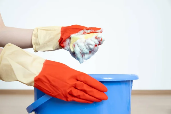 Manos en guantes para limpiar. Una esponja con un detergente se espumó en una mano sobre un cubo azul. — Foto de Stock