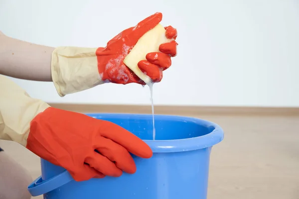 Manos en guantes para limpiar. Una esponja con un detergente se espumó en una mano sobre un cubo azul. — Foto de Stock