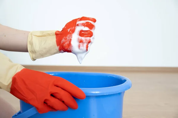 Manos en guantes para limpiar. Una esponja con un detergente se espumó en una mano sobre un cubo azul. — Foto de Stock