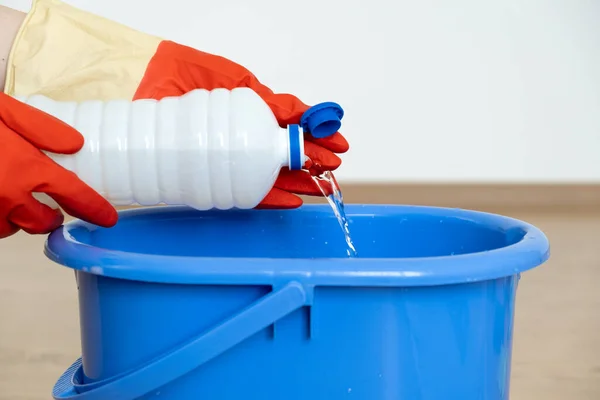 Χέρια σε γάντια για τον καθαρισμό χύστε ένα καθαριστικό για επιφάνειες καθαρισμού πάνω από ένα μπλε κουβά. Εικόνα Αρχείου