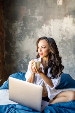 Minyon esmer beyaz kız yatakta rahatlatıcı çatı katında dizüstü bilgisayar ile