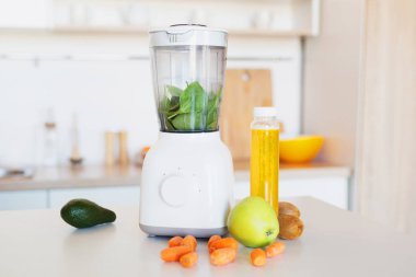 Blender, elma, havuç, avokado ve şişe suyu beyaz mutfak masasında