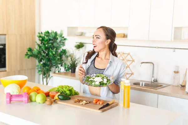 Petite and fit brunette caucasian girl eating salad during cooking at kitchen