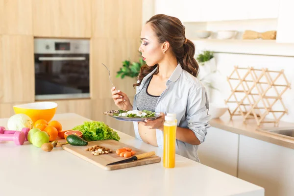 Petite and fit brunette caucasian girl eating salad during cooking at kitchen