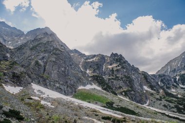 kar, çimen ve bulutlu gökyüzü ile kayalık manzara