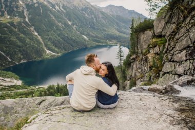 Norveç fiyordu içinde kaya kenarında oturan genç çift