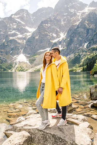 Young couple in yellow raincoats on walk inTatra Mountains near lake Morskie Oko, Poland