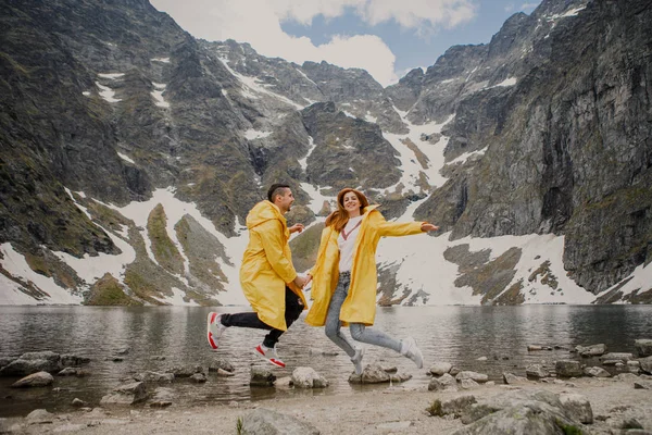 Young couple in yellow raincoats on walk inTatra Mountains near lake Morskie Oko, Poland