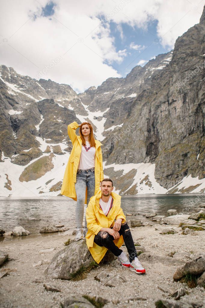 Young couple in yellow raincoats on walk inTatra Mountains near lake Morskie Oko, Poland