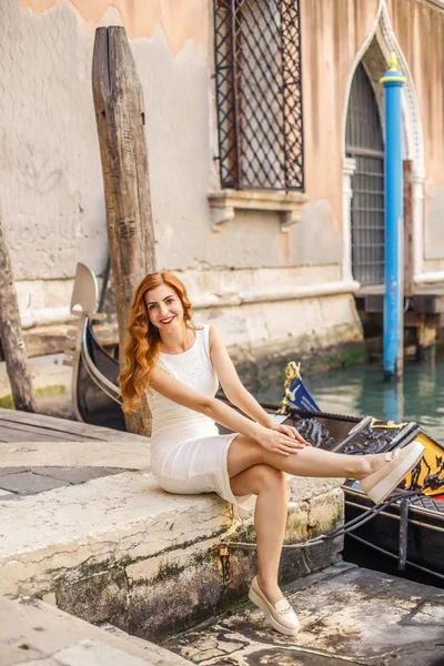 Gondol yakınındaki iskele üzerinde oturan çekici Kızıl saçlı kadın. Venedik.