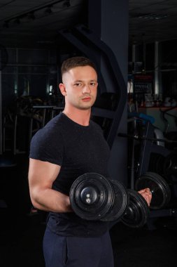 Genç Erkek atlet vücut içinde karanlık bir spor salonunda dumbbells ile egzersizleri yapıyor mavi spor giyim