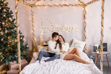 Genç güzel çift yatakta Noel ağacı arka plan üzerinde oturan ve gülümseyen