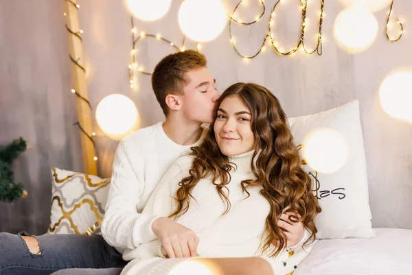 年轻美丽的夫妇坐在圣诞树的背景上的床上 面带微笑 — 图库照片