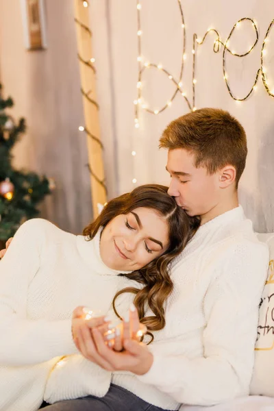 年轻美丽的夫妇坐在圣诞树的背景上的床上 面带微笑 — 图库照片