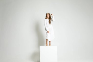 beyaz bir küp üzerinde bir beyaz odada ayakta beyaz giysili genç güzel kızı