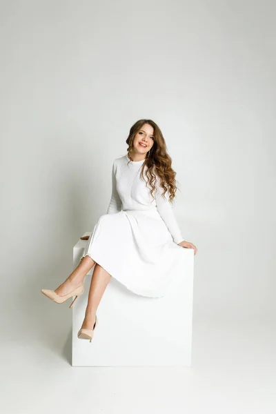 young beautiful girl in white clothes sitting in a white room on a white cube