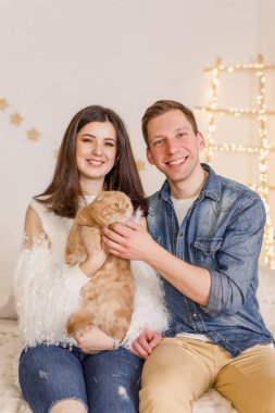 Genç güzel çift ile kedi parlak odasında yatağın üstüne oturuyor